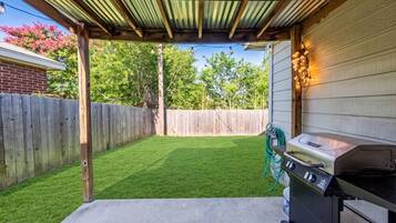 A backyard with a grill, a wooden fence, and a pergola structure.