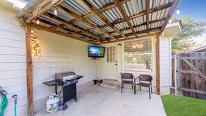 A covered patio with a grill, chairs, and a TV.