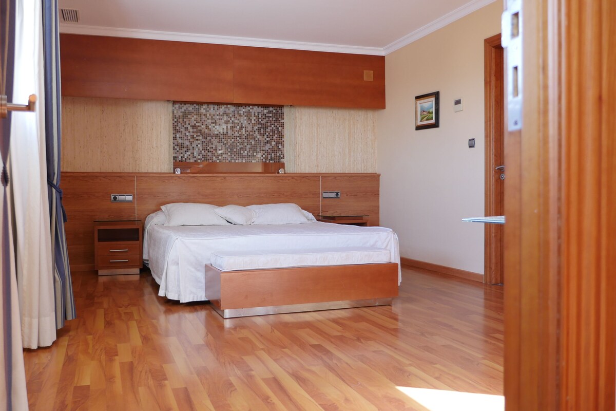 Ein Schlafzimmer mit einem hölzernen Bett, einem Nachttisch, einer Kommode und einem Fenster mit einem gemusterten Vorhang.