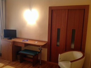A room with a wooden desk, a television, a bench, and a door. - Rusadir (Melilla)