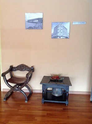 Una habitación con piso de madera, una silla de madera oscura, una pequeña mesa con un cuenco de fruta y dos cuadros en la pared.