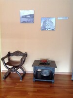 Una habitación con piso de madera, una silla de madera oscura, una pequeña mesa con un cuenco de fruta y dos cuadros en la pared.