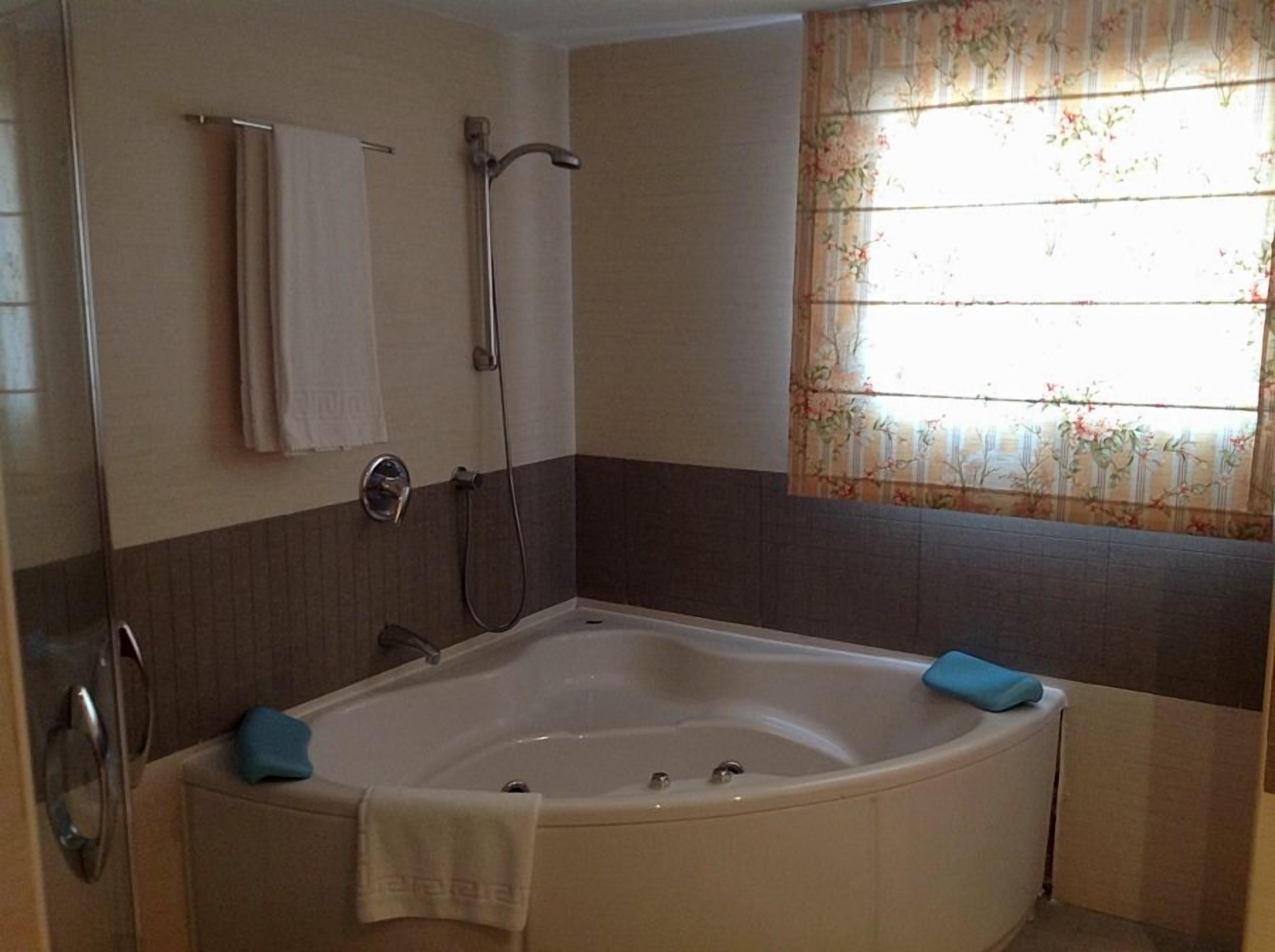 A bathroom with a bathtub, a shower, and a window with floral curtains.