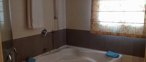 A bathroom with a bathtub, a shower, and a window with floral curtains.