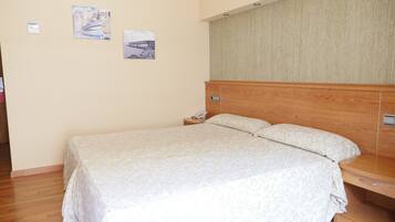Una cama bien hecha con una colcha estampada con motivos florales, un cabecero de madera y una mesita de noche con un teléfono.