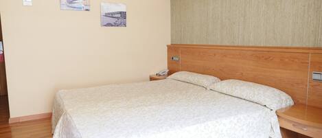 Una cama bien hecha con una colcha estampada con motivos florales, un cabecero de madera y una mesita de noche con un teléfono.