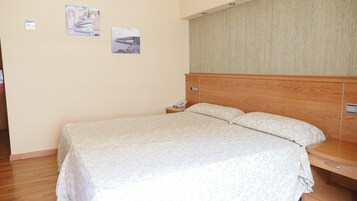 Una cama bien hecha con una colcha estampada con motivos florales, un cabecero de madera y una mesita de noche con un teléfono.