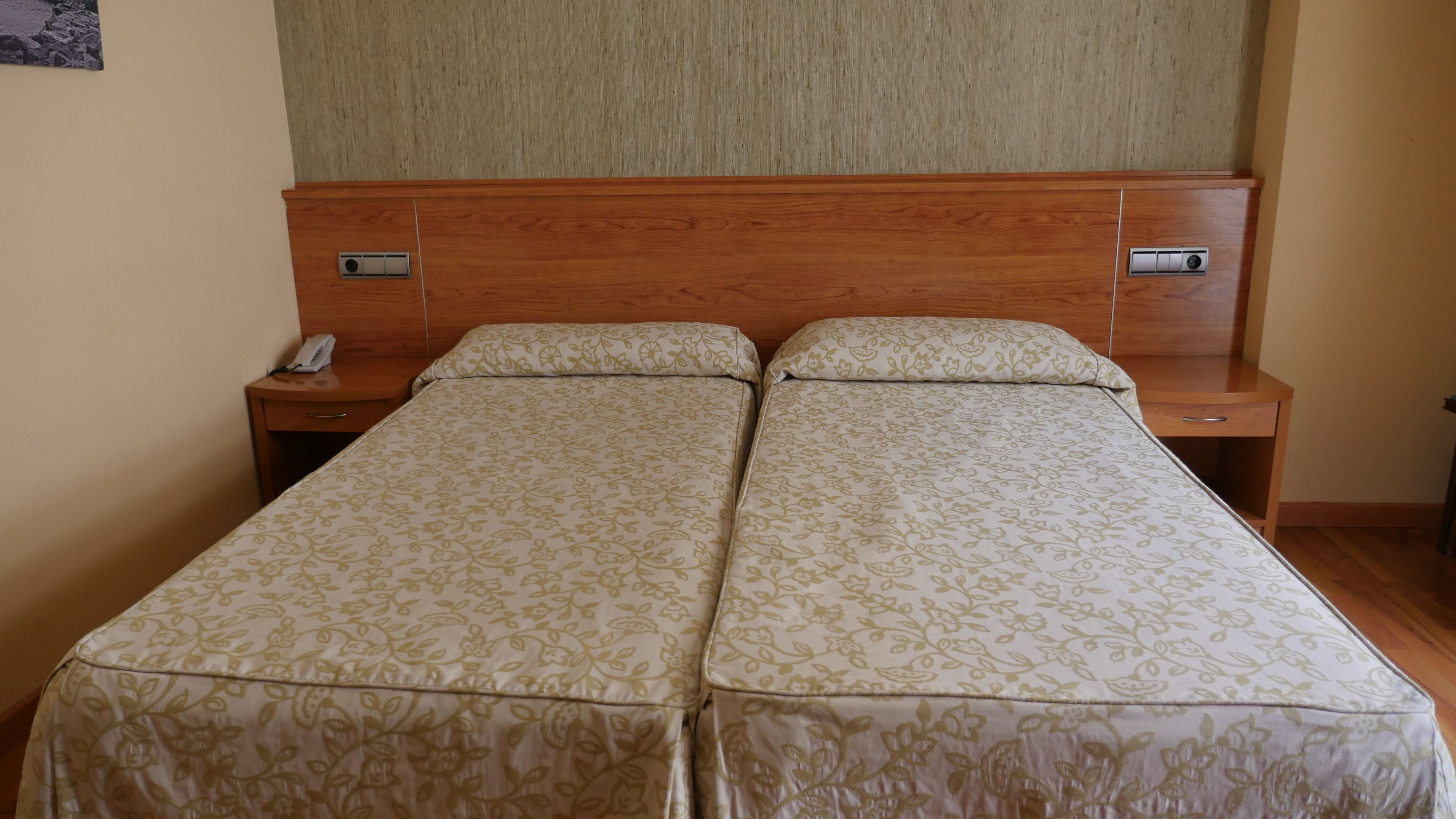 Un lit double avec une literie à motifs floraux, une tête de lit en bois, des tables de chevet avec des lampes et un téléphone sur l’une des tables.