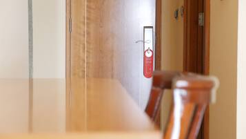 Habitación de hotel con una puerta de madera, un cartel rojo con un símbolo y texto, y una silla en primer plano.
