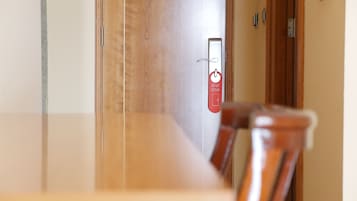 Habitación de hotel con una puerta de madera, un cartel rojo con un símbolo y texto, y una silla en primer plano.