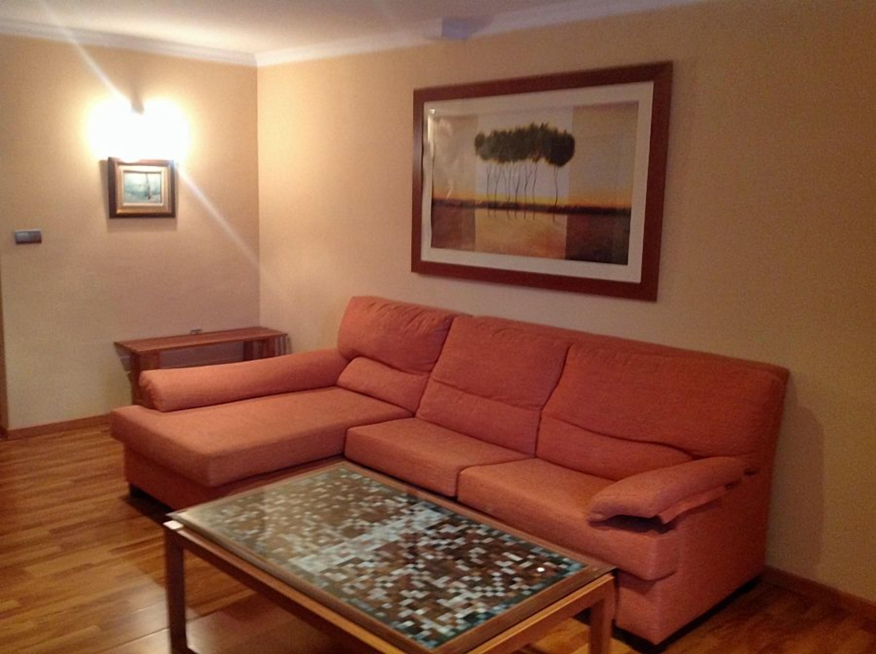 Una sala de estar con un sofá modular, una mesa de centro, un cuadro enmarcado y una lámpara de pared.