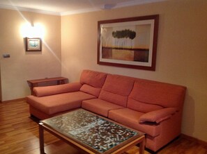 A living room with a sectional sofa, a coffee table, a framed painting, and a wall-mounted light fixture. - Rusadir (Melilla)