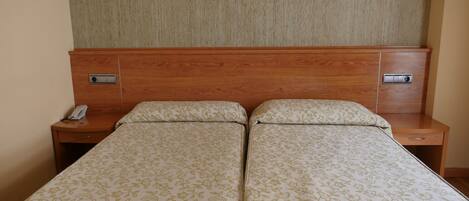 Cama doble con ropa de cama de estampado floral, cabecera de madera, mesitas de noche con un teléfono y un interruptor de luz.