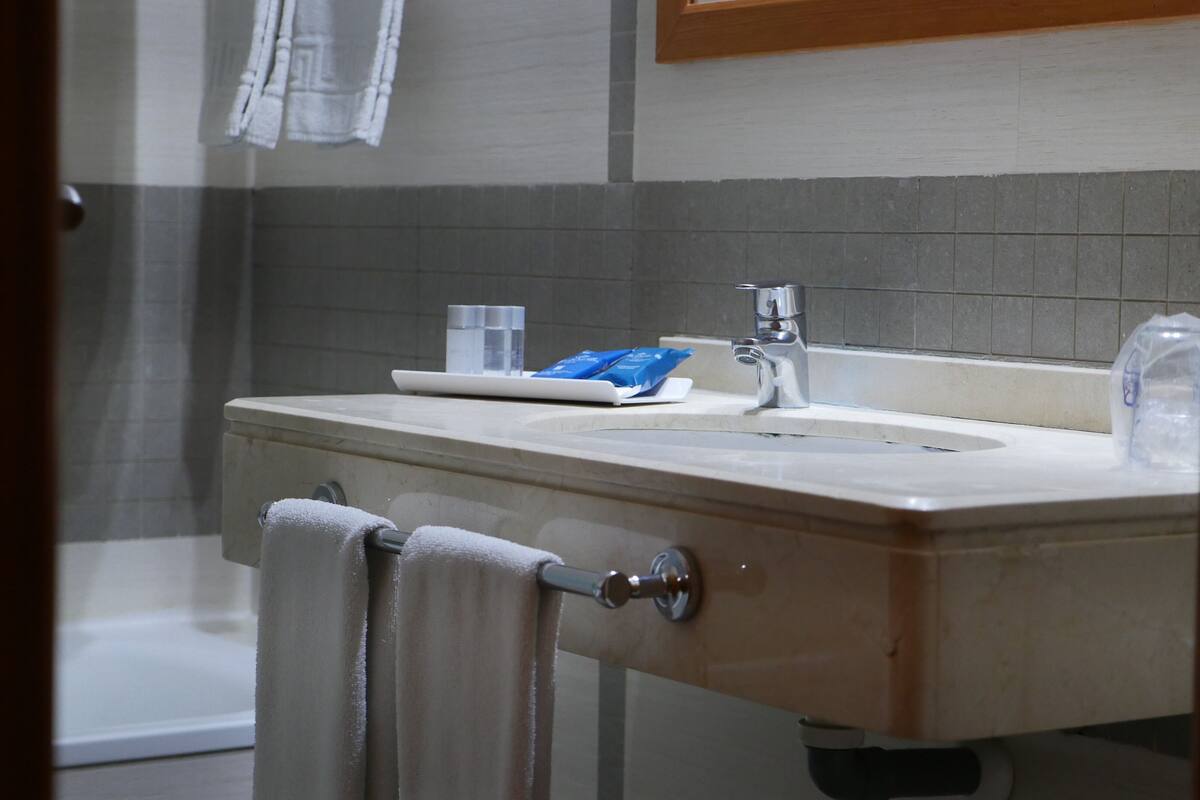 Ein Badezimmer mit Waschbecken, Spiegel, Handtuchhalter und Duschbereich.