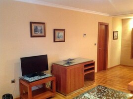 Una sala de estar con un televisor sobre un mueble bajo, un armario de madera y un tapete estampado.