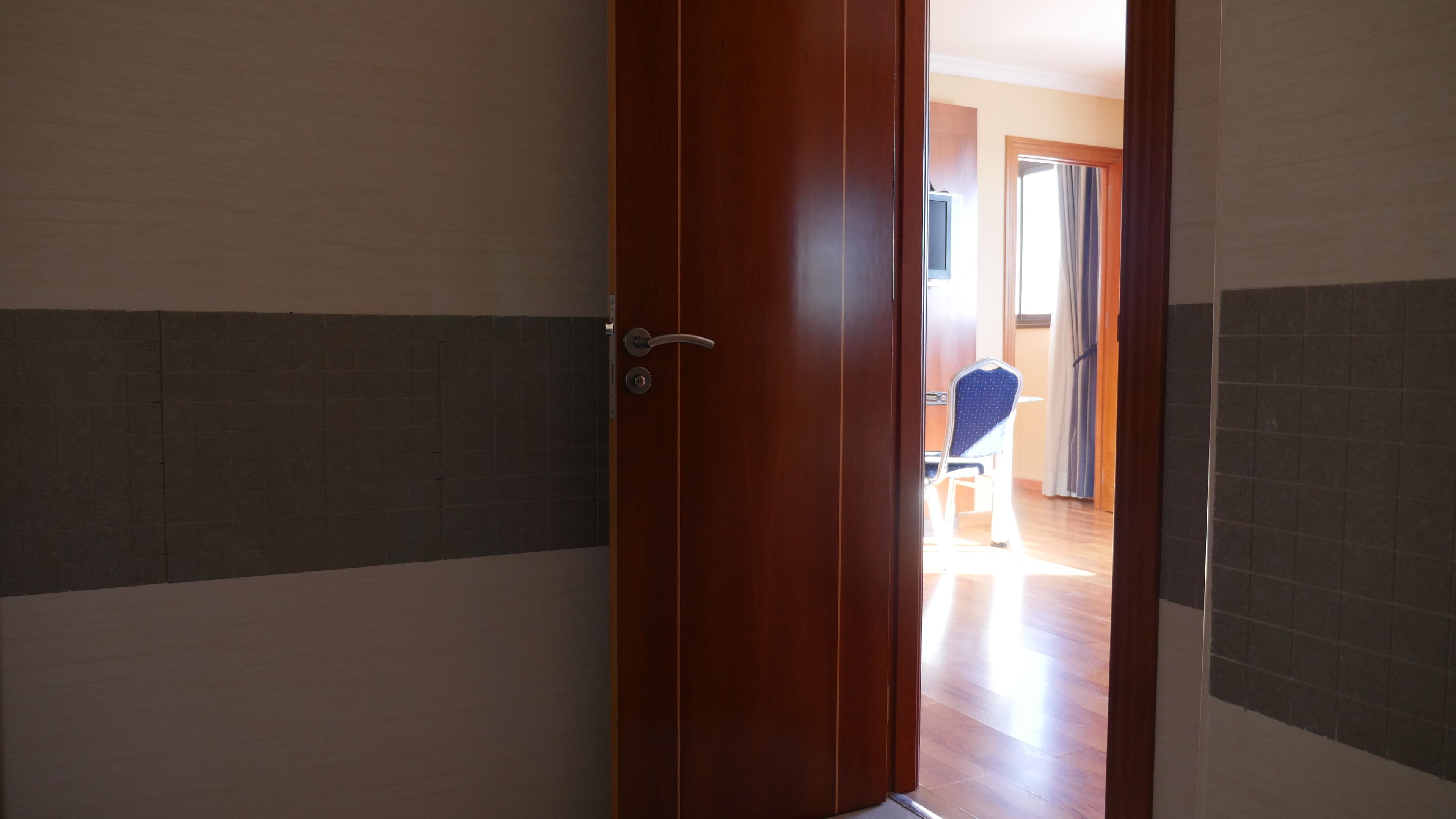 Una puerta de madera que da a un cuarto con paredes de baldosas y una silla a la vista al fondo.