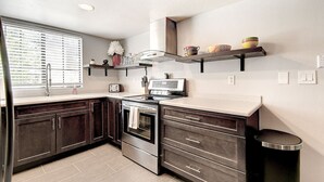 A modern kitchen with dark wooden cabinets, a stainless steel stove, and a window with blinds.