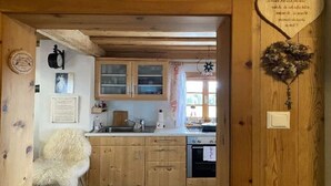 Een landelijke keuken met houten kastjes, een witte stoel en een hartvormige decoratie aan de muur.