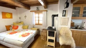 Een gezellige kamer met een bed, een klein houten tafeltje, een hond en een keukenhoek.