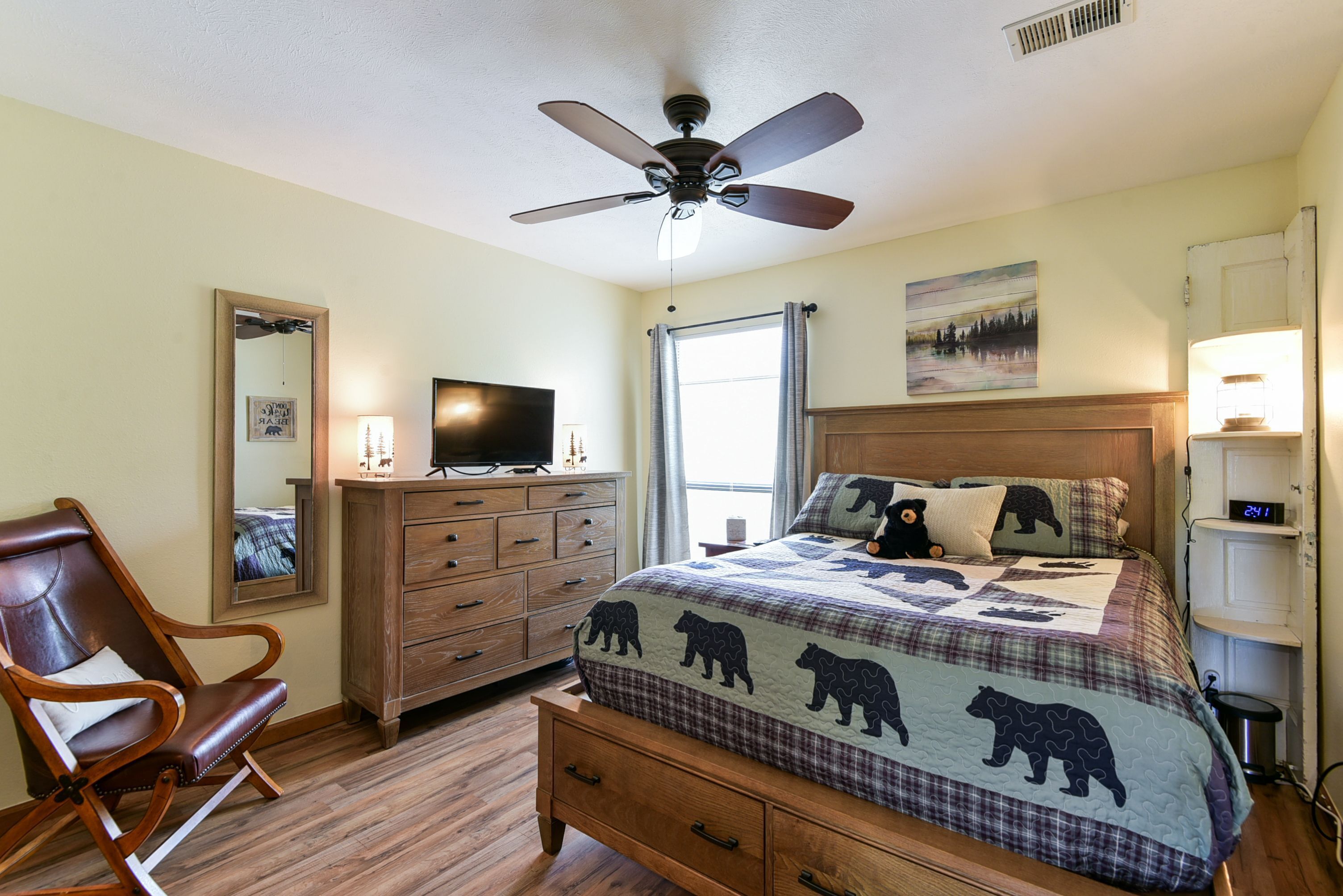 A bedroom with a bed, a chair, a dresser, a television, and a ceiling fan.