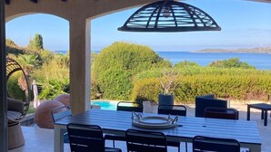 Un patio exterior con una mesa y sillas, un lámpara colgante y vistas al mar y vegetación.