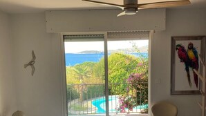 Un dormitorio con cama, una silla, ventilador de techo y vistas a una piscina y follaje.