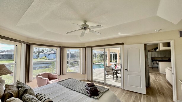 A bedroom with a large bed, a ceiling fan, and a view of a backyard patio.