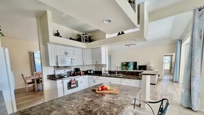 A modern kitchen with white cabinetry, a granite countertop, and a dining area with a chair.