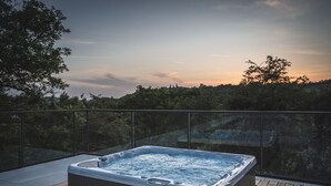 Un bain à remous sur une terrasse en bois, avec une balustrade en verre, donnant sur une zone boisée.