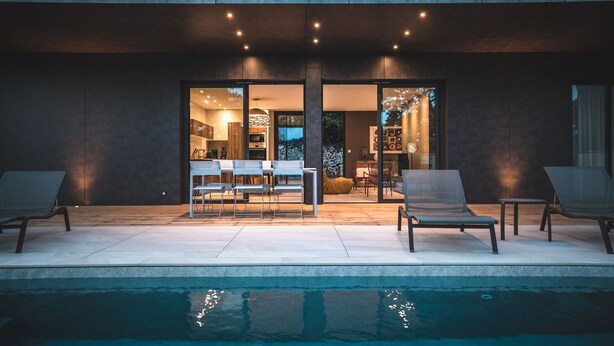 Un espace piscine extérieur moderne, doté de chaises longues et d’une porte vitrée donnant accès à un espace intérieur bien éclairé.
