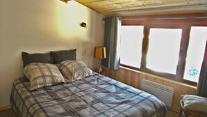 Une chambre à coucher avec un lit, une table de chevet, une lampe et une fenêtre avec des rideaux.