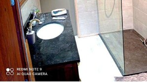 Une salle de bain avec un plafond en bois, une cabine de douche en verre et un lavabo équipé de produits de toilette.
