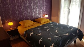 Cozy bedroom with a bed, nightstand, and lamp, set against a vibrant floral wallpaper.