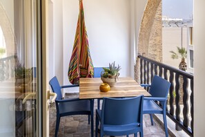 A balcony with a wooden table, blue chairs, a colorful striped umbrella, and a potted plant. - CASA FELIZ TWO BEDROOM A406 (Germasogeia)