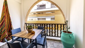 Ein Balkon mit Holztisch und -stühlen, einem Blumentopf und einem farbenfrohen Streifenstoff.