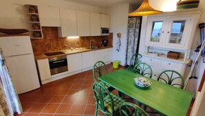 A compact kitchen with white cabinets, a wooden countertop, and a green dining table with chairs. - Spacious apartment in seafront condo (Portu Maga)