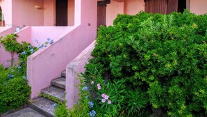 A pink building with a covered staircase and a lush green bush in front. - Spacious apartment in seafront condo (Portu Maga)