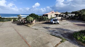 A coastal property with a white car parked in the driveway, a view of the ocean, and a house with a red roof. - Spacious apartment in seafront condo (Portu Maga)