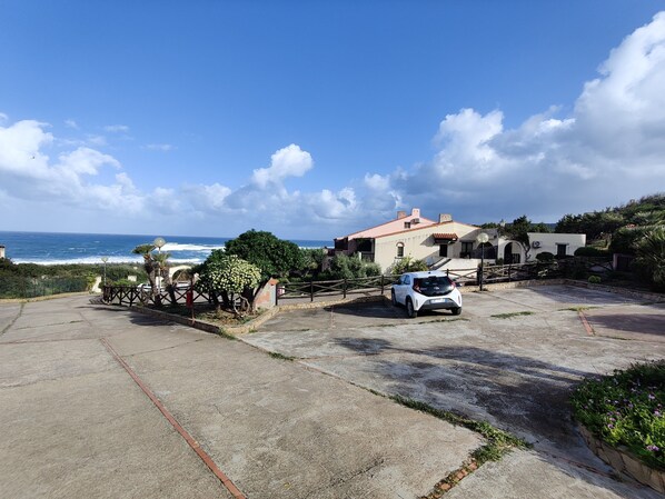 A coastal property with a white car parked in the driveway, a view of the ocean, and a house with a red roof.