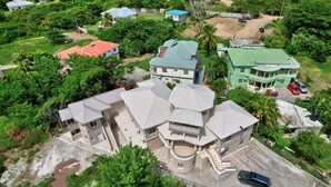 A large, multi-story house with a central courtyard, surrounded by lush greenery and other residential buildings. - Quaint one bedroom unit steps away from beach access (Saint George)