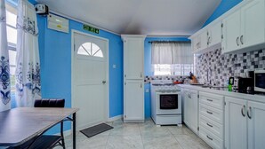 A compact kitchen with white cabinets, a stove, and a microwave. There's a fire exit sign above the door, and a window with a view of the outside. - Quaint one bedroom unit steps away from beach access (Saint George)