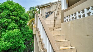 A staircase with beige steps and white railings, leading to a building with a beige exterior and a decorative white pattern on the wall. - Quaint one bedroom unit steps away from beach access (Saint George)