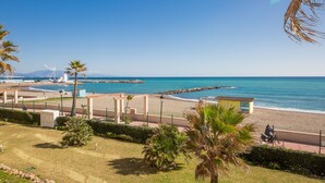 Vista costera con playa, un faro y un rompeolas rocoso.