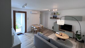 A modern living room with a grey sofa, a wooden dining table, and a TV. - Mi-Re-La House in the vicinity of historic Villa Manin - Codroipo (CODROIPO)