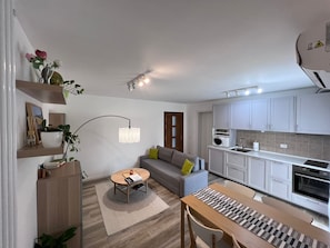 A compact living space with a sofa, a dining table, a kitchen area, and a pendant light.