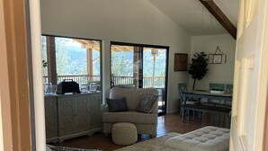 A cozy living room with a sofa, ottoman, and a dining area with a table and chairs. - Lake Naci Rendezvous with Lake Views (Bradley)