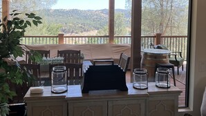 A room with a large window overlooking a scenic landscape, a wooden table with chairs, and a cabinet with decorative doors. - Lake Naci Rendezvous with Lake Views (Bradley)