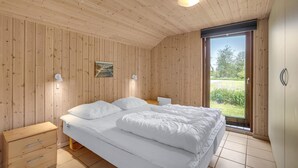A bedroom with a wooden ceiling, a bed with white bedding, two bedside tables, and a window with a view of greenery. - Beautiful home in Væggerløse with WiFi (Væggerløse)