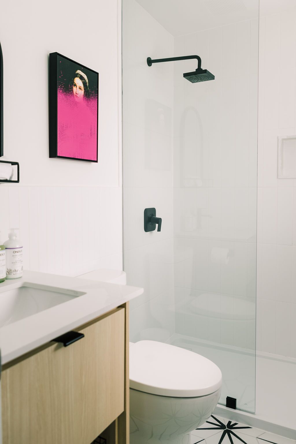 Un baño moderno con cabina de ducha de vidrio, inodoro blanco y lavamanos con mueble de madera.
