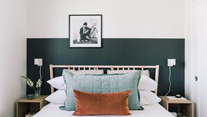 Un lit bien fait, avec une tête de lit en bois, deux tables de chevet et un tableau encadré accroché au mur.
